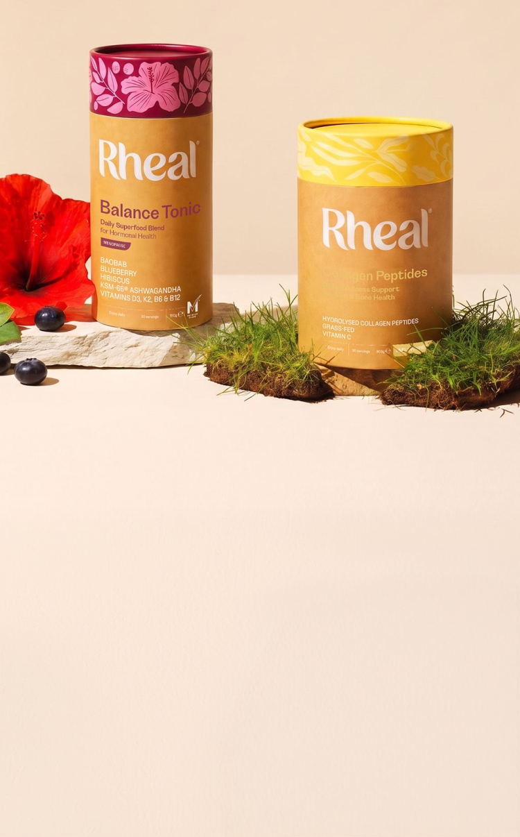 Rheal Balance Tonic Menopause and Rheal Collagen tubs surrounded by hibiscus, blueberries and moss